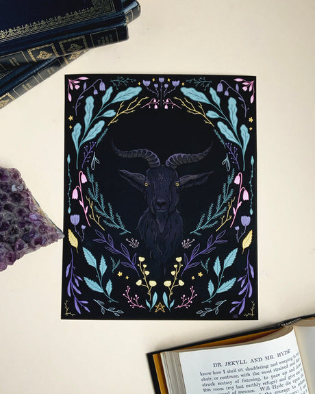 A black and white print featuring a stylized illustration of a goat with horns, surrounded by colorful floral patterns and leaves, with a decorative border.