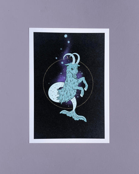 A 5x7 print of a hand-drawn illustration featuring a goat with a mermaid's tail, set against a dark background with a celestial pattern.